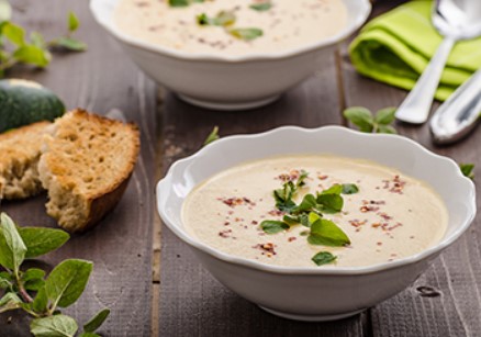Crema de calabacín con hierbas, pan y verduras a su alrededor